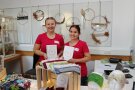 Zwei Frauen in einheitlichen Shirts präsentieren Buch in die Kamera.