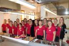 Gruppe von Frauen in roten Shirts vor Küchenzeile.