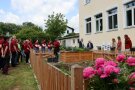Personengruppe in einheitlichen T-Shirts steht an Gartenzaun mit Beeten.