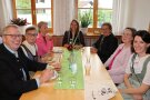 Sieben festlich gekleidete Personen an tisch in Speisesaal unterhalten sich in lockerer Atmospähre.