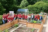 Eine Gruppe von Menschen steht entlang eines Holzzauns in einem Hausgarten mit Beeten.