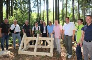 Personengruppe steht im Wald um ein Dachstuhl-Gestell aus Holz.