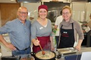 Zwei Frauen und ein Mann in einer Küche beim Zubereiten von Speisen