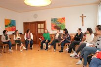 Gruppe von Frauen auf Stühlen im Kreis sitzend, in der Mitte sitzt eine Frau mit einer Gitarre.