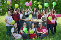 Personengruppe auf einer Wiese, die Personen halten Luftballons in die Höhe