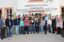 IZahlreiche Personen in großem Halbkreis vor Gebäude mit Aufschrift Landwirtschaftsschule Pfarrrkirchen stehend,.