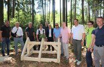Personengruppe steht im Wald um ein Dachstuhl-Gestell aus Holz.