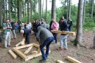 Gruppe von Personen im Wald baut mit Balken kleinen Dachstuhl.