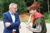 Mann als Robin Hood verkleidet mit Pfeil und Bogen begrüßt Mann im Anzug.