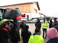 Mann referiert im Freien neben landwirschaftlicher Maschine, Zuhörer stehen im Kreis um ihn herum.